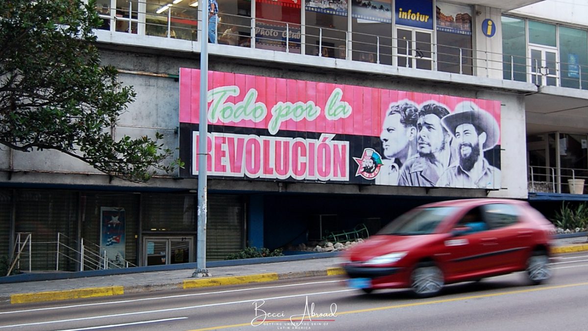 Bil kører forbi et stort skilt med teksten "todo por la revolución" (Alt for revolutionen) i Havana, Cuba