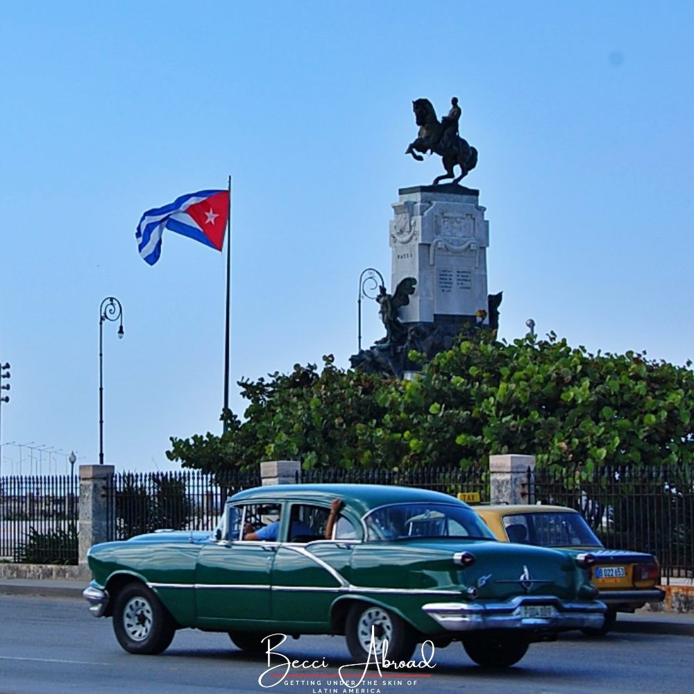 En gammel Amerikanerbil kører på Malcón havnepromenaden med det cubanske flag i baggrunden