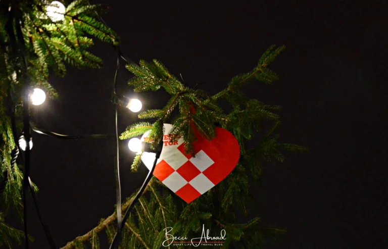 A red and white woven julehjerte on a fir branch lit by string lights